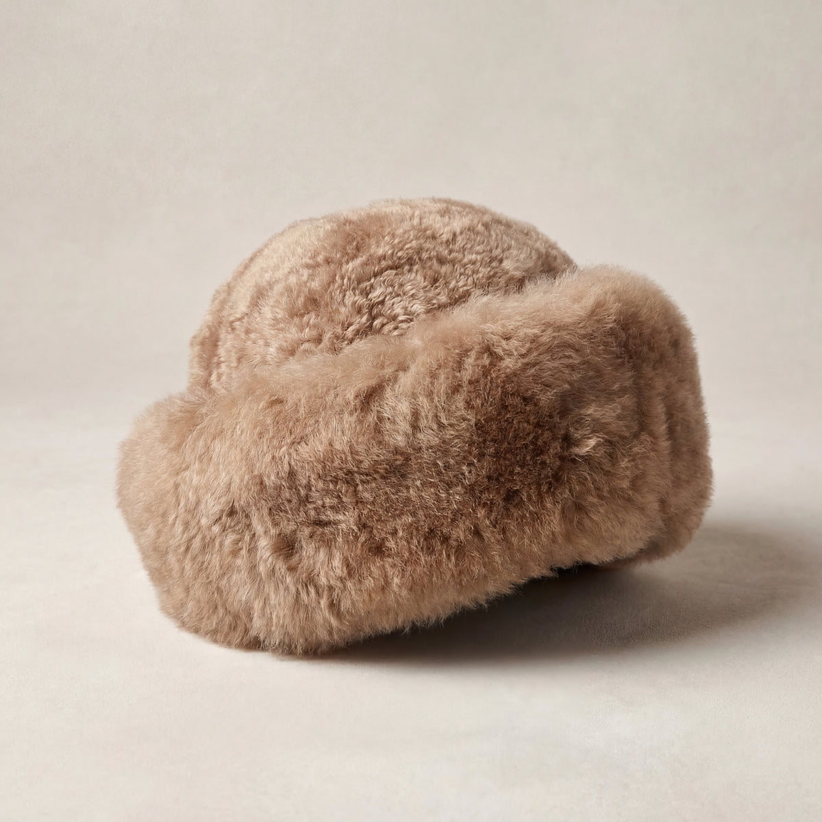 Taupe baby alpaca fur hat with a rounded silhouette on a warm neutral studio background