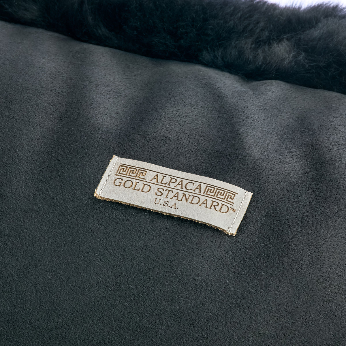 Back of black baby alpaca fur cushion with Alpaca Gold Standard label