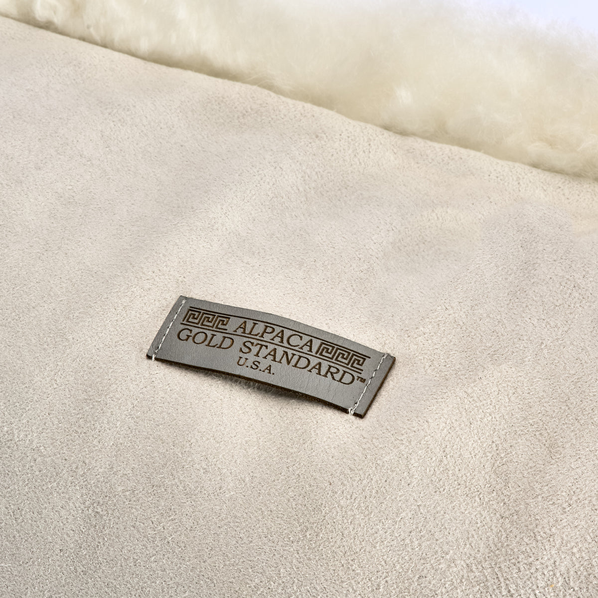 Back of ivory white baby alpaca fur cushion with Alpaca Gold Standard label